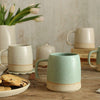 Close up of mint green mug on table with white mugs in background