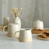 Habulous small stoneware mug off-white in front of large white mug and table setting of white stoneware ceramics