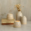 Two lit white tealight holders on old stack of books with white vases in background