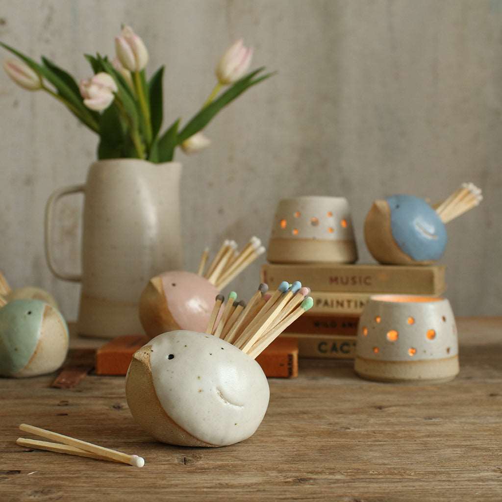Collection of pastel match pot birds on table with tealights, old books and a vase of flowers.