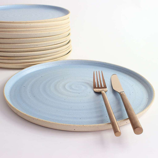 Blue dinner plate with copper cutlery next to stack of plates