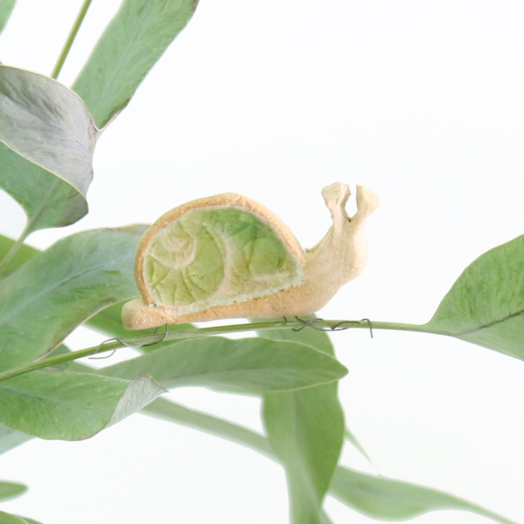 small ceramic and glass emerald green snail plant decoration, with thin wire wrapped around house plant stem