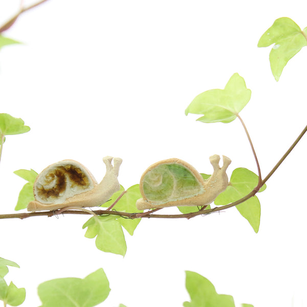 two small ceramic and glass brown and green snail plant decorations, with thin wire wrapped around house plant stem