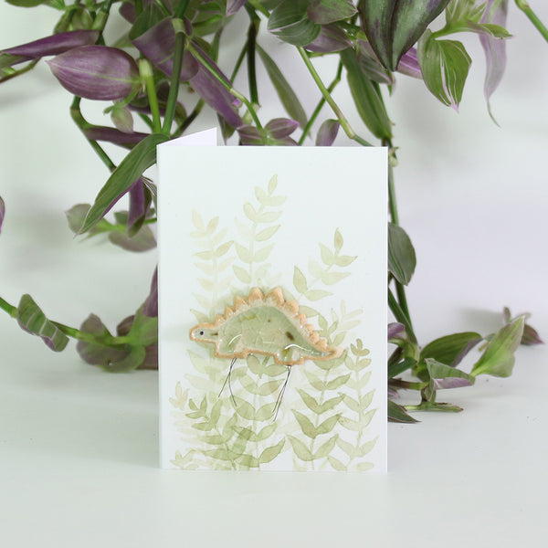 small ceramic and glass hazel stegosaurus on gift card with watercolour leaves