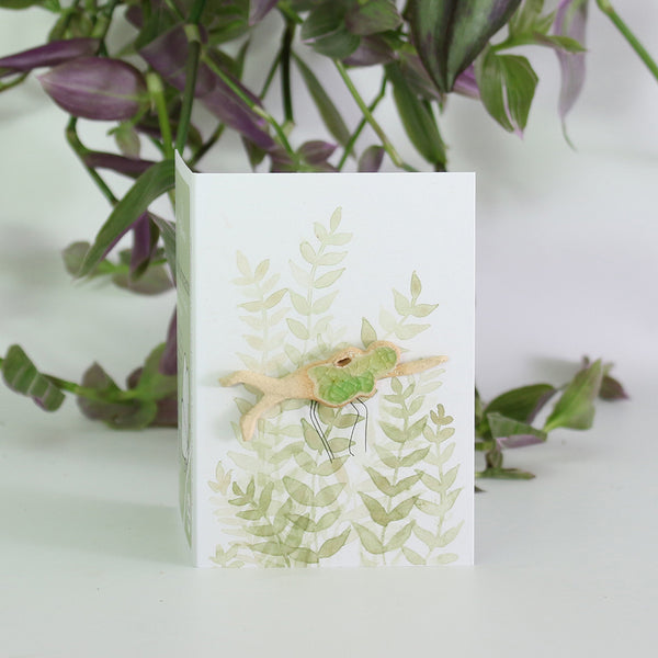 small ceramic and glass swimmer with emerald green cap and costume on gift card with watercolour leaves