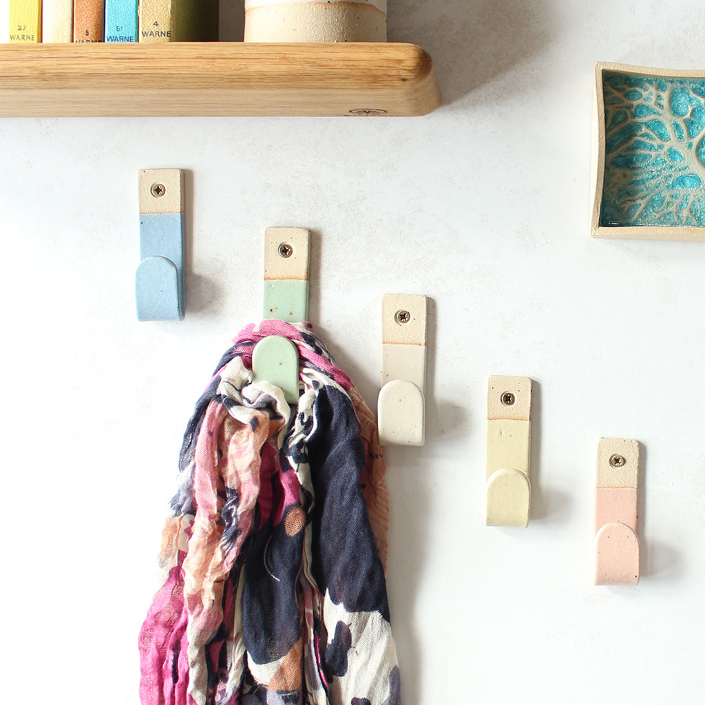 Five pastel coloured stoneware wall hooks with scarf hanging off one hook, surrounded by decor