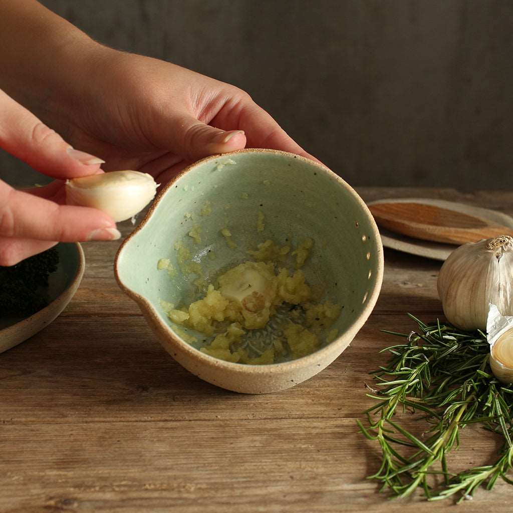 A green herb bowl being held up in the process of grating garlic cloves