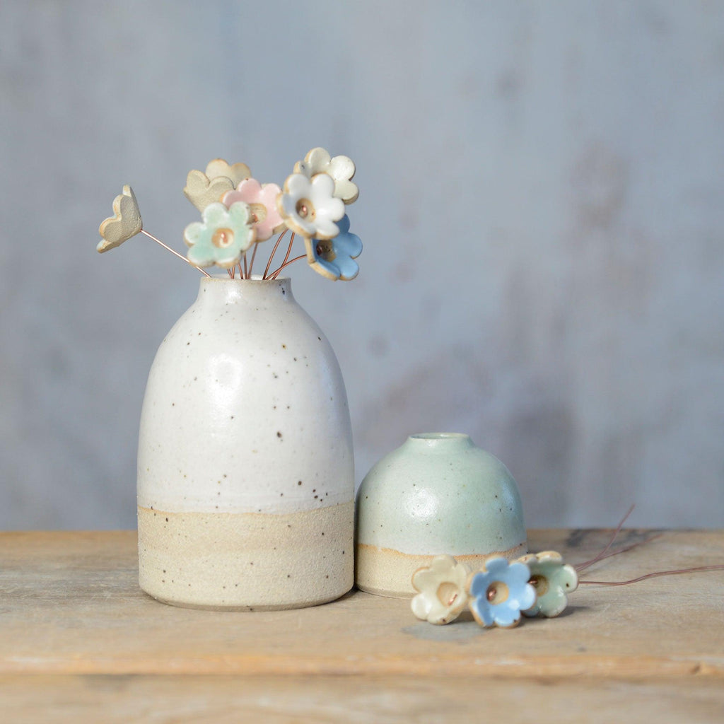 White vase of pastel ceramic flowers next to mini green vase