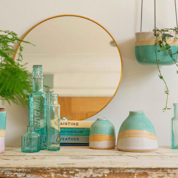 Mantlepiece with blue glass bottles, Shoreline vases and vintage books. Above hangs the matching shoreline planter next to the circular mirror